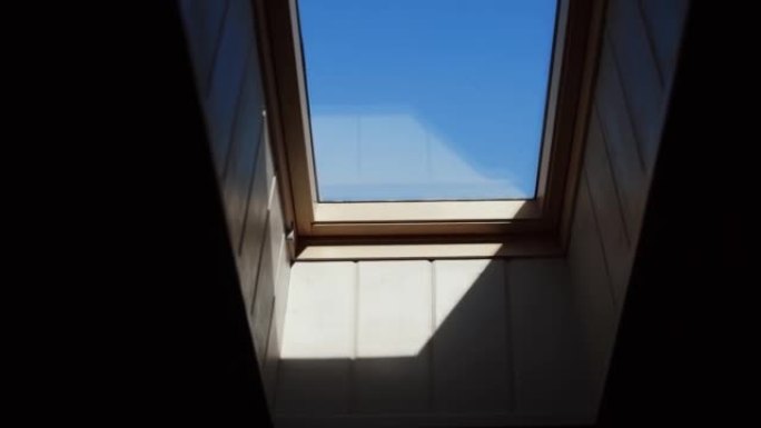 在房子阁楼上的小窗户上可以看到晴朗的蓝天和一缕阳光