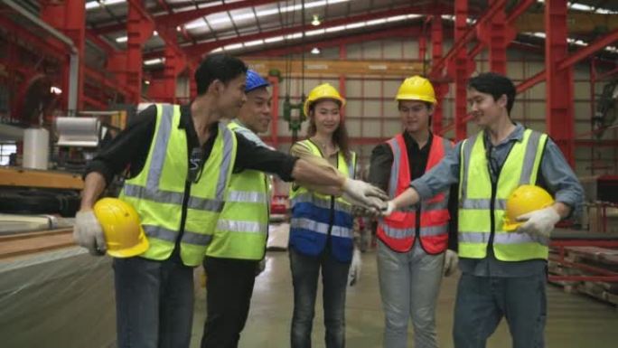 一群站在微笑的亚洲工程师和工人戴着安全安全帽，在工厂一起工作成功后，双手齐齐。