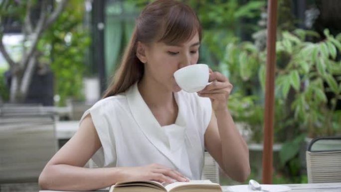 年轻女子看书，喝一口咖啡，微笑着。