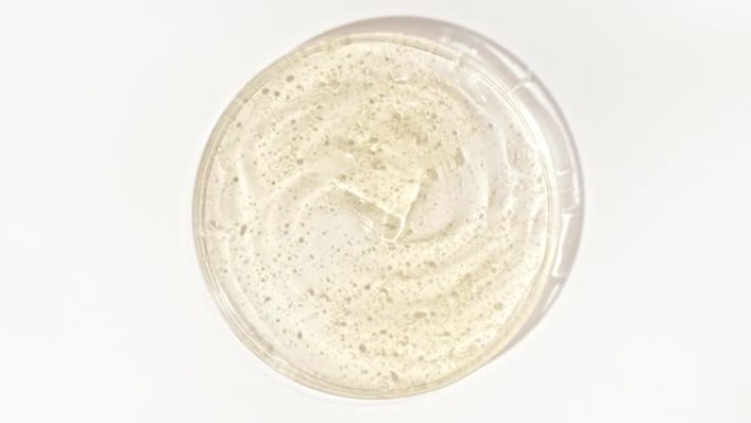 在Petri玻璃碗中旋转带有气泡的透明黄色化妆品凝胶液。宏丸血清、乳膏、透明质酸。有机化妆品，药品。
