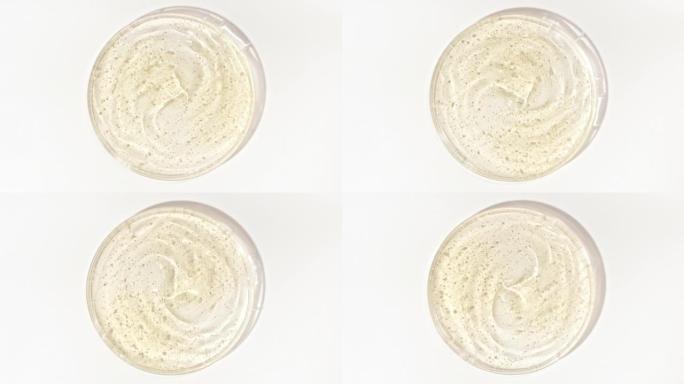 在Petri玻璃碗中旋转带有气泡的透明黄色化妆品凝胶液。宏丸血清、乳膏、透明质酸。有机化妆品，药品。