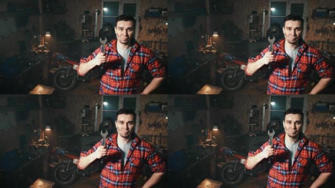 男机械师微笑着在车间车库背景上展示一把大扳手