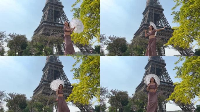 巴黎美丽的年轻少女在埃菲尔铁塔的背景下，穿着浪漫主义风格的优雅长裙，带着一把雨伞从阳光下行走，微笑着