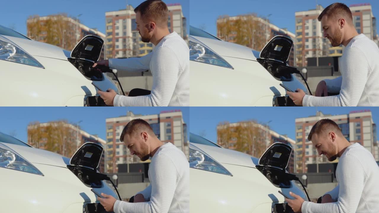 皮肤白皙的男司机将电动汽车连接到电源系统，为汽车电池充电，并通过智能手机控制充电过程
