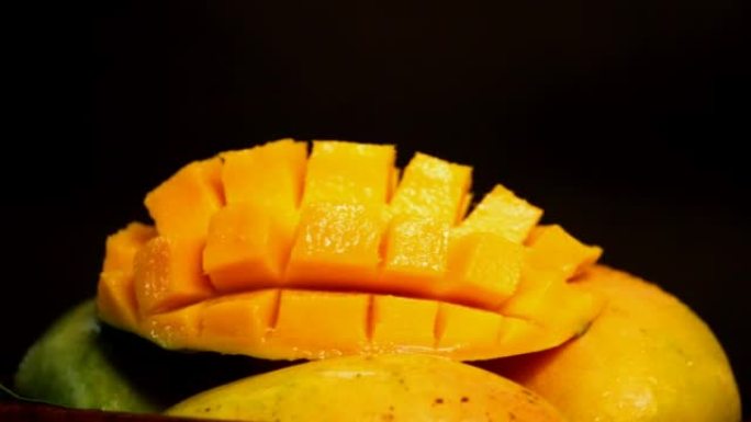 芒果在托盘上旋转，通过在黑色背景上将立方体切成骰子形状，将新鲜美味的成熟芒果切成薄片，
