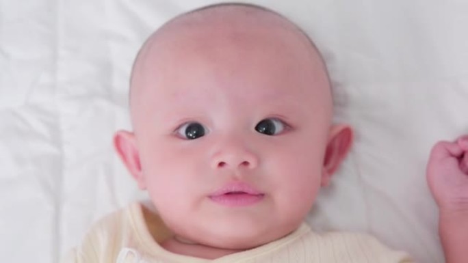 脸部特写肖像可爱的亚洲新生婴儿躺在白色床上玩耍看着相机笑着笑脸。天真的小新婴儿可爱。父母身份和母亲节