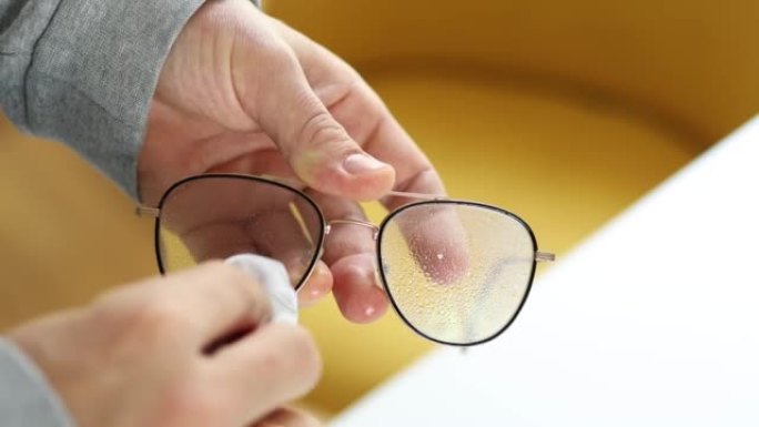 一个男人的手用清洁液喷涂眼镜并用布擦拭的特写镜头