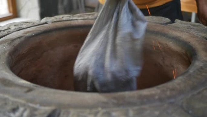 一位亚美尼亚面包师将煤从一个袋子倒入一个里面有火的石头tonir中。将木炭倒入烤面包和埃里温·霍罗瓦