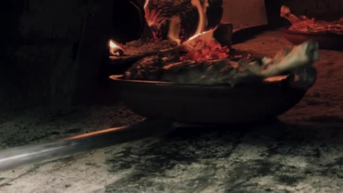 钢刀片从燃木烤箱中取出粘土板中的烤羊肉