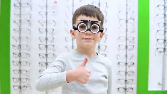 小男孩站在带有眼镜镜框的橱窗的背景上，并带有用于选择隐形眼镜的装置