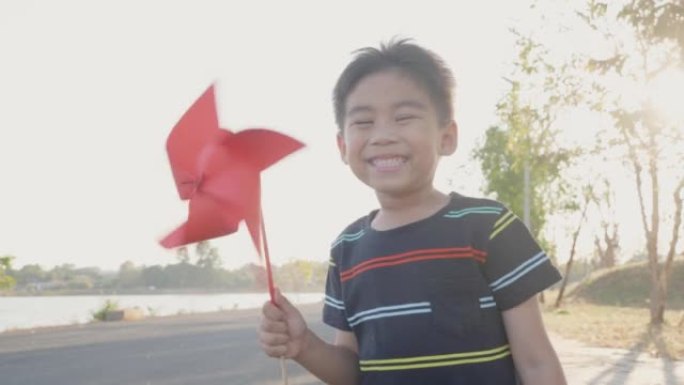 亚洲男孩玩风车，快乐小男孩微笑在麦田里拿着小风轮或风车玩具在公园花园的夏日
