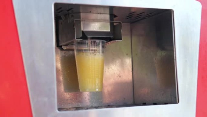 复古自动机器用果汁填充塑料玻璃。街头自助服务机器将饮料倒入玻璃杯中。