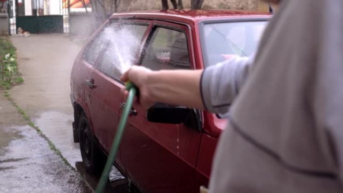 一名高级男子手里拿着软管，在后院洗车。