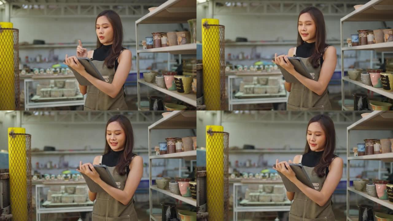 亚洲女陶艺家用围裙手将她的粘土雕刻产品放在架子上等待烤箱烘烤，亚洲女小企业陶瓷车间老板微笑着自豪地展