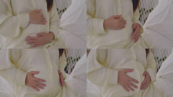 一位亚洲孕妇轻轻地抚摸着她的肚子，等待着她一生中最美好的时刻