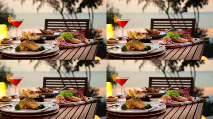 日落时分，浪漫的晚餐放在木制桌子上，有海、地平线、天空背景。豪华酒店或度假村的高级餐厅。烤三文鱼和西