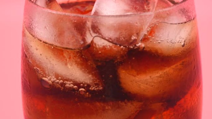 可口可乐在粉红色背景的冰镇玻璃中产生气泡。