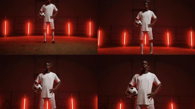 运动黑人男子手持足球，晚上独自站在足球场上，艺术红灯