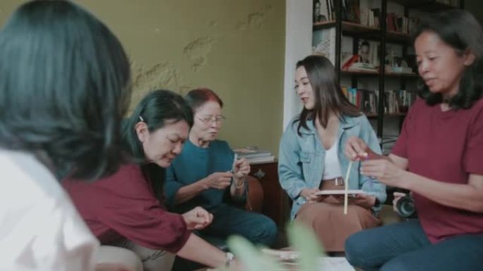 一群泰国资深成年人和他们的表弟在周末在读书俱乐部尝试制作手工纸花时交谈和分享。