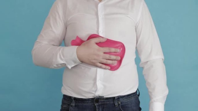 一个穿着白衬衫的男人在他的肚子上放了一个红色的加热垫。消化道健康问题的概念，胃痛，特写