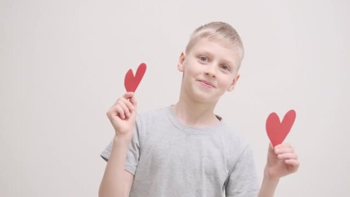 一个开朗的男孩的肖像，手里拿着心形，微笑着。情人节的人、情感和感受的概念。2月14日。情人节。快乐，