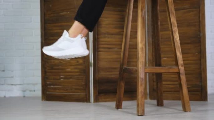 面目全非的女人坐在高高的木凳上挥舞着脚。模型展示白色舒适的鞋类。