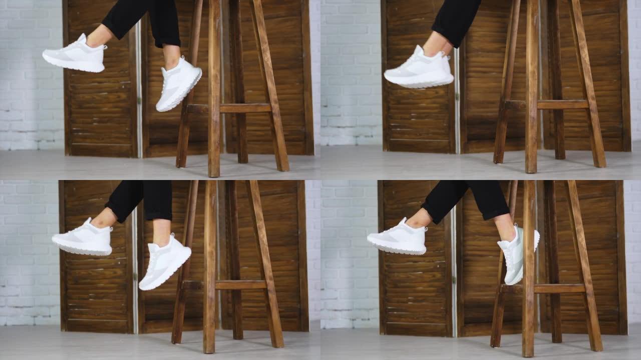 面目全非的女人坐在高高的木凳上挥舞着脚。模型展示白色舒适的鞋类。