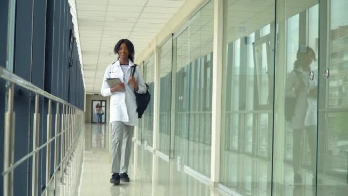 非洲裔美国学生实习生带着平板电脑在医院散步。新型现代化的全功能医疗设施。医学、保健和人的概念