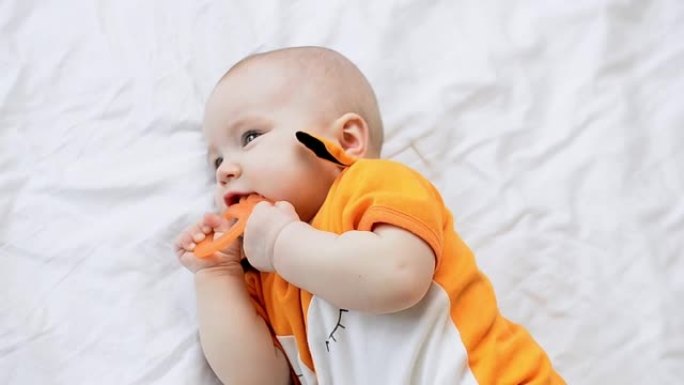 可爱的婴儿躺在白色床上，咬着牙胶特写。婴儿长出第一颗牙齿。