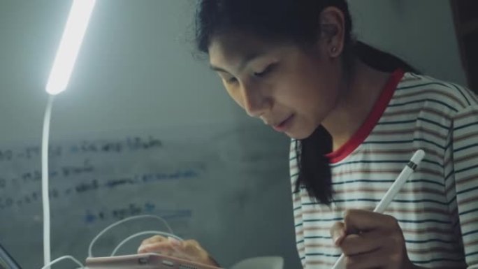 亚洲女孩在家里的餐桌上做作业时使用数字平板电脑和铅笔，生活方式理念。