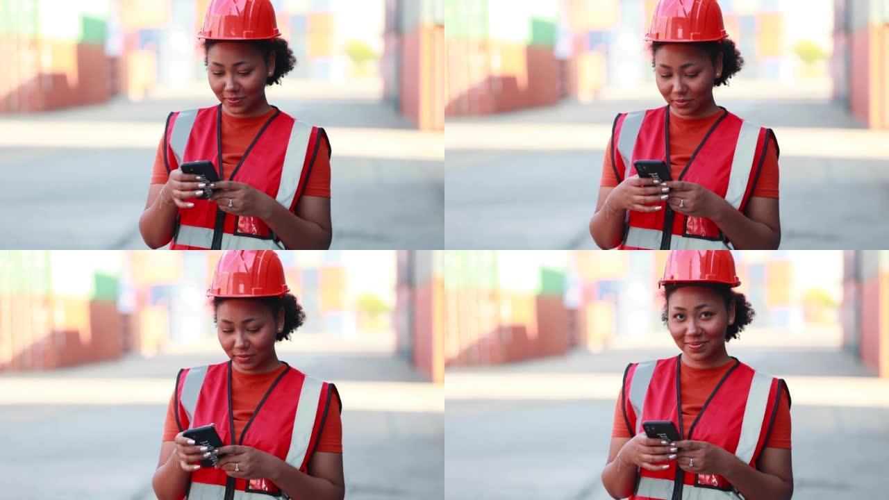 通过智能手机在线工作。黑人女码头工人控制从仓库集装箱堆场的货物中装载集装箱箱。海运和承运人保险概念。