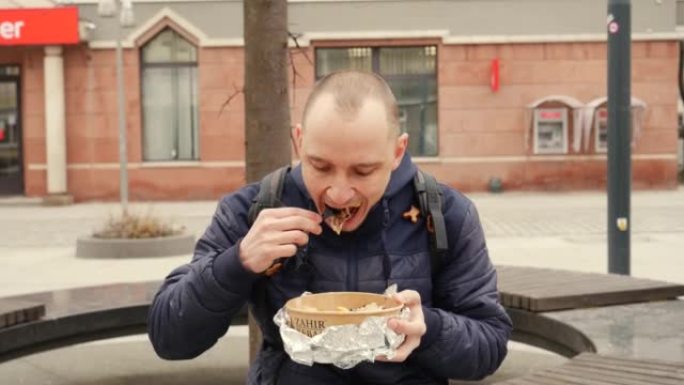 街上的男人坐在吃外卖食品盒，里面有烤肉串肉，沙拉和一次性餐具中的炸土豆片