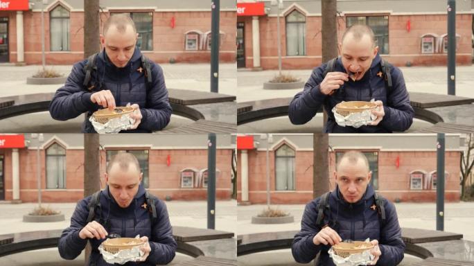 街上的男人坐在吃外卖食品盒，里面有烤肉串肉，沙拉和一次性餐具中的炸土豆片
