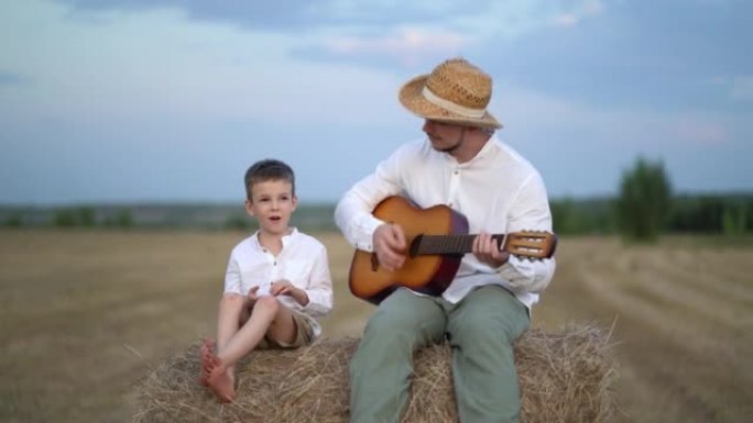 小男孩和他的父亲在野外的hay bale弹吉他。