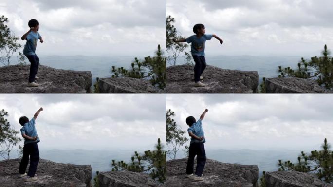 ฺ男孩高举双臂站在悬崖顶上。