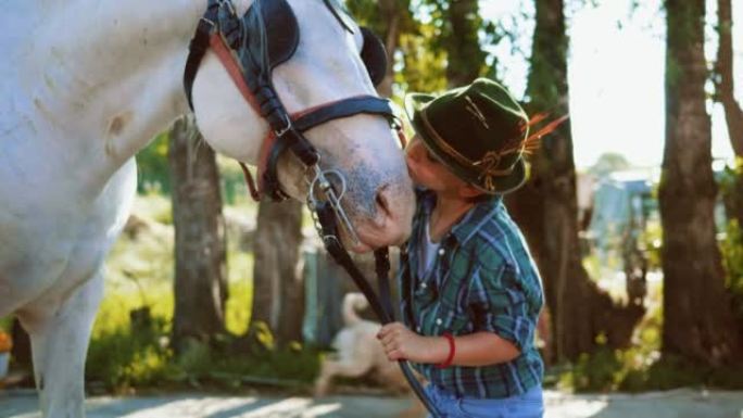 一个戴着帽子的小男孩的真实特写镜头正在爱抚和亲吻一匹白马