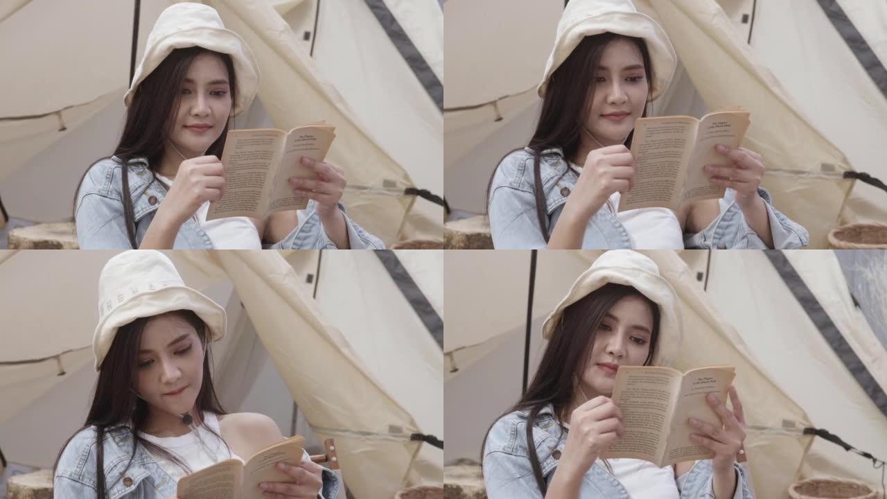 年轻女子在露营地前帐篷的椅子上看书