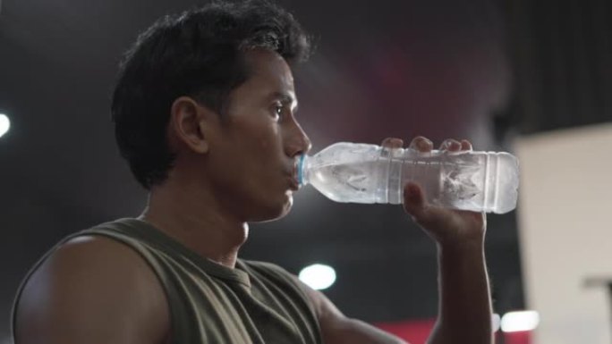 穿着运动服的亚洲男子的肖像累了，出汗了，在健身房用瓶子喝水。健康的男运动员在健身后补充水分平衡后放松