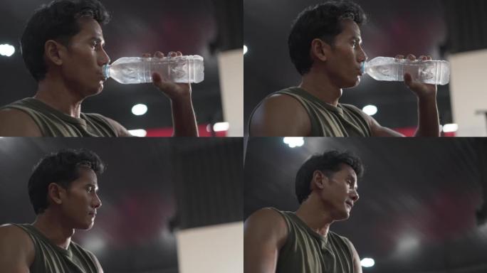 穿着运动服的亚洲男子的肖像累了，出汗了，在健身房用瓶子喝水。健康的男运动员在健身后补充水分平衡后放松