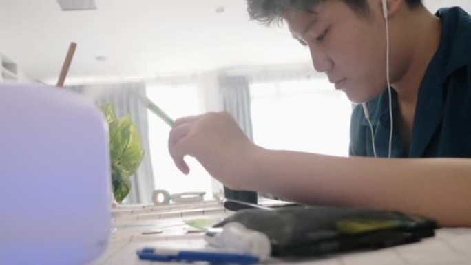 亚洲男孩在家用蒸喷机附近的餐桌学习在线课程，社交疏远的生活方式理念。