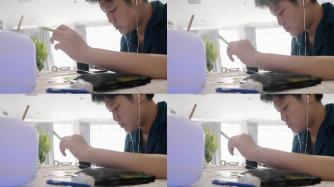 亚洲男孩在家用蒸喷机附近的餐桌学习在线课程，社交疏远的生活方式理念。