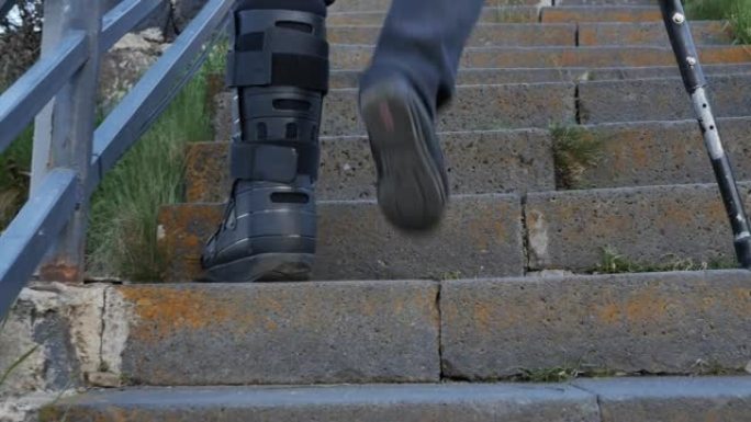 左腿受伤的人靠在一只拐杖上爬楼梯，将塑料康复紧身胸衣放在断腿上。