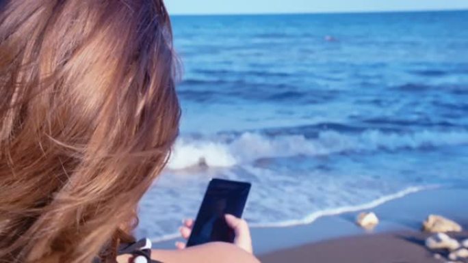 悲伤的孤独女人坐在海边的椅子上，用手机思考，翻看前男友的照片和视频