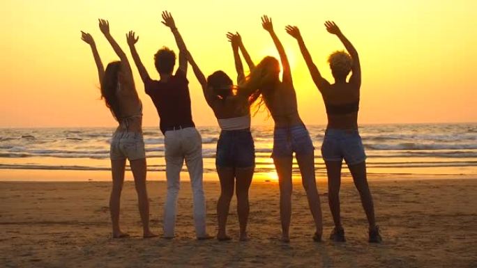 一群快乐的人坐在空旷的日落海滩上，向太阳挥手致意