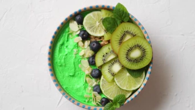 绿色冰沙或酸奶碗。新鲜的猕猴桃，蓝莓，酸橙和杏仁片