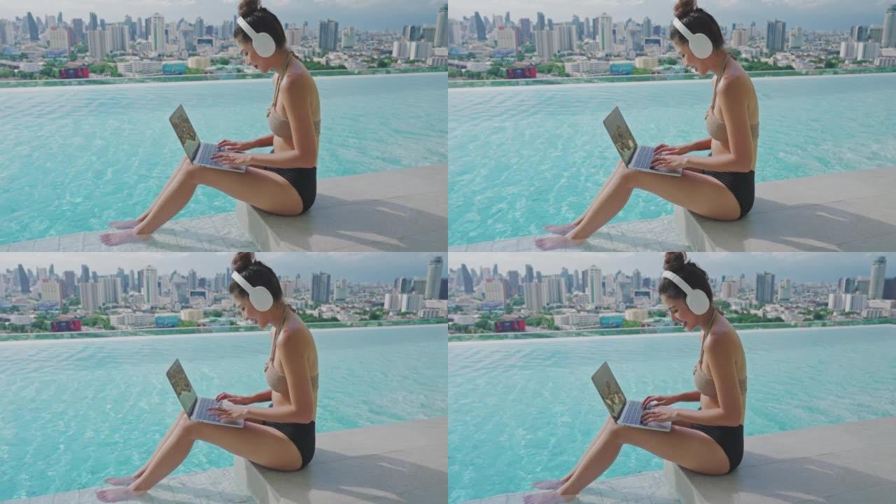 年轻的亚洲女性在夏天使用笔记本电脑坐在游泳池附近