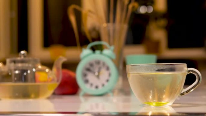 用柠檬和透明玻璃茶壶泡茶。白色厨房桌子上的杯子里的天然凉茶
