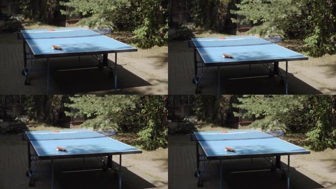 蓝色折叠乒乓球桌，放在阳光下的轮子、球拍和球上。