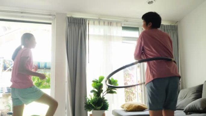 快乐的亚洲儿童在家里窗户附近一起锻炼，男孩玩呼啦圈。