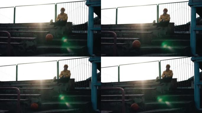 男孩坐在观众看台上，一个球在他旁边滚落。慢动作镜头